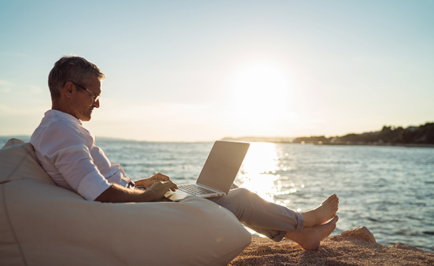 Man in beanbag chair holding laptop on beach at sunset