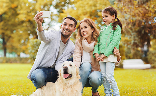 Man, woman, girl and dog pose for selfie outdoors in park