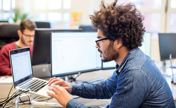 Man with afro hairstyle working on laptop at desk in office