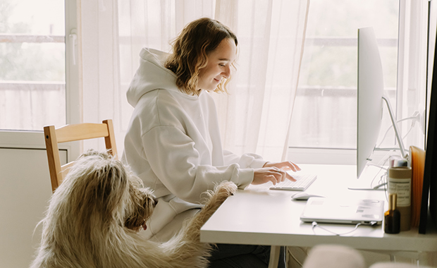 Woman at desk looking at computer with dog next to her
