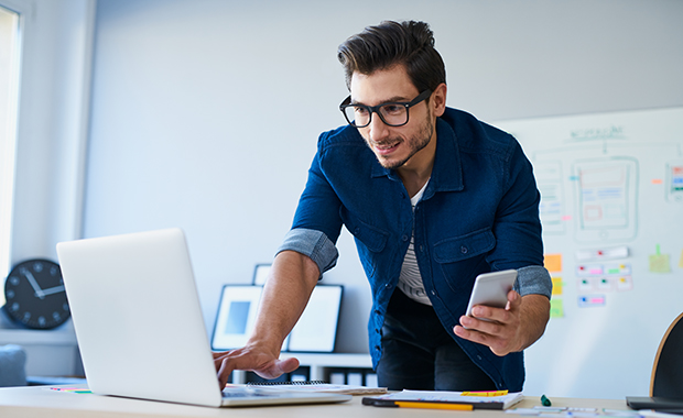 Web designer working on laptop while holding smartphone