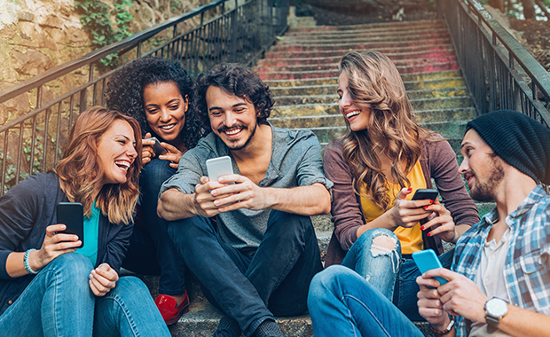 Multi-ethnic group of friends with smart phones sitting on stairs outdoors
