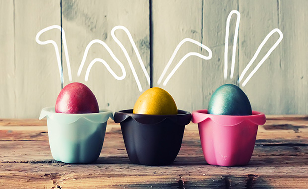 Three colored eggs in cups with bunny ears above