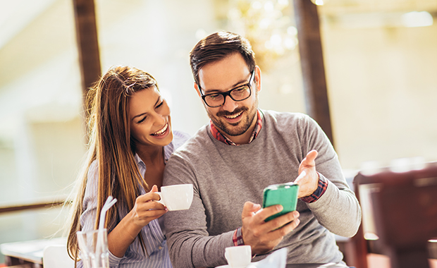 Smiling man showing smartphone to woman holding coffee cup