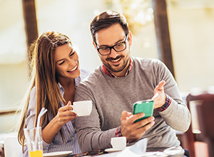 Smiling man showing smartphone to woman holding coffee cup