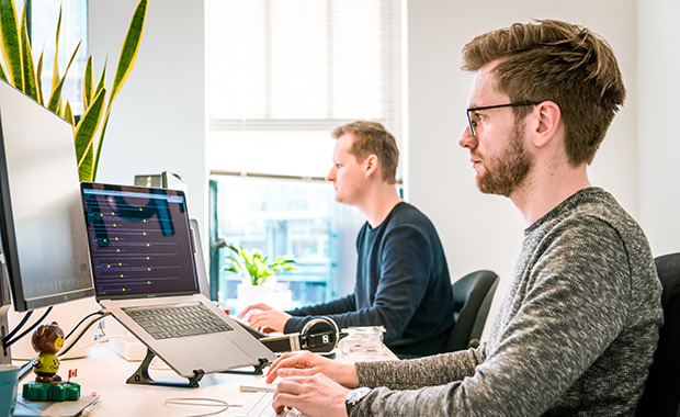 Man in office looking at laptop and large computer screen