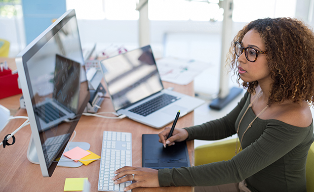 Woman writing on graphic tablet and looking at computer screen