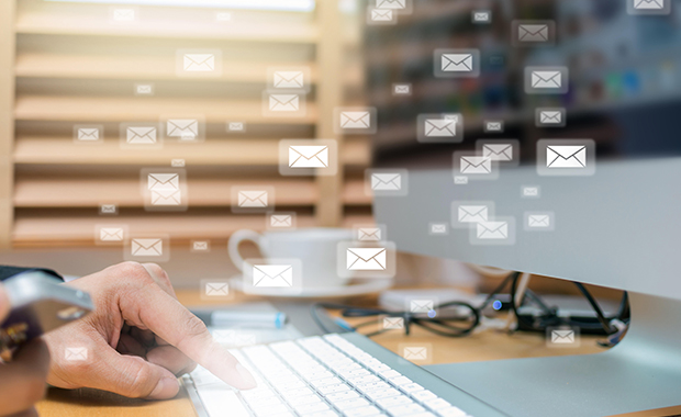 Hands typing on computer keyboard with email icons floating in air