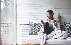 Woman sitting on couch reading emails on smartphone
