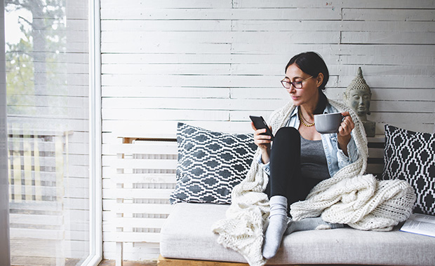 Woman sitting on couch reading emails on smartphone