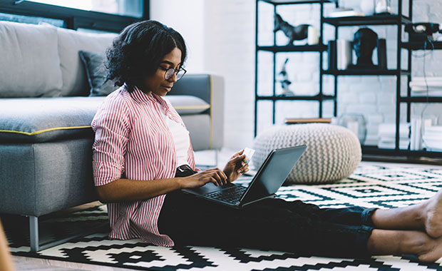 Woman sits on living room floor shopping on laptop