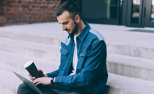 Man sitting on steps outdoors looking at laptop