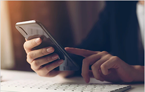 Hand holding a smartphone above a computer keyboard
