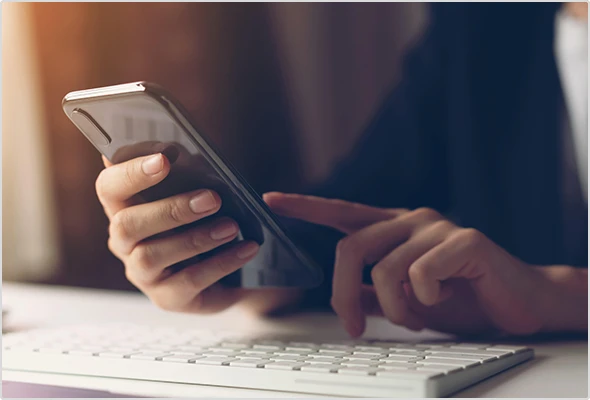 Hand holding a smartphone above a computer keyboard