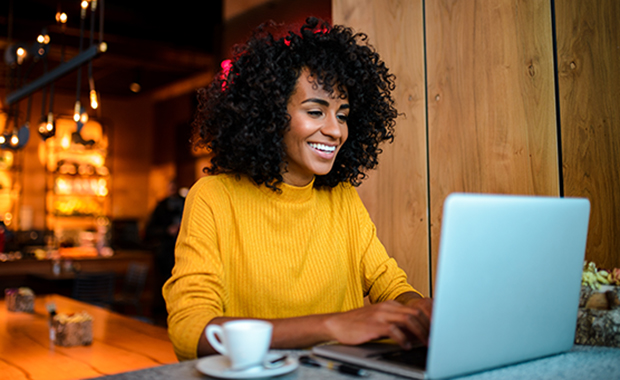 Woman in yellow sweater sits in cafe working on laptop