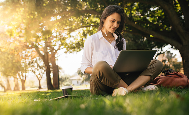 Woman sits in grass at sunset looking at laptop