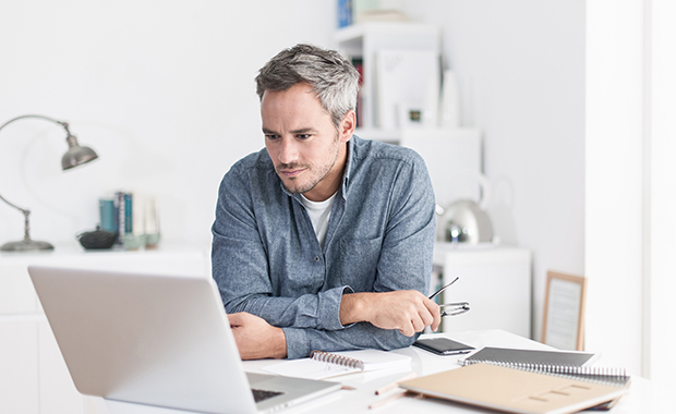 Man with grey hair looks at laptop in home office with white furnishings