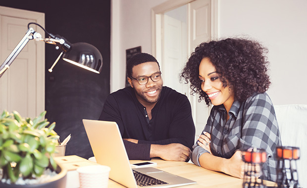 Woman and man sit at desk looking at laptop and smiling