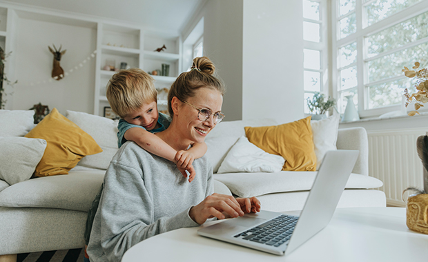 Woman works on laptop on coffee table with young boy looking over shoulder