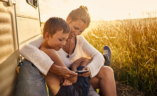 Mother and son sit outside camper and look at smartphone