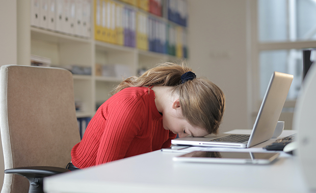 Woman sitting at desk resting forehead on laptop keyboard