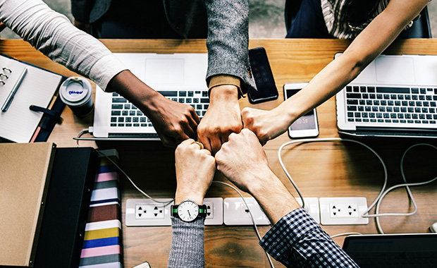 5 hands bumping fists over table with computer equipment