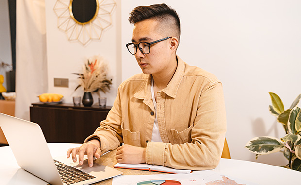 Young man uses laptop on table cluttered with papers