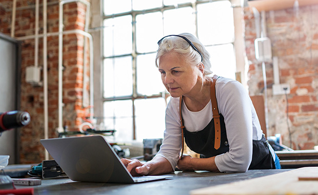 Senior woman looking at laptop in woodworking workshop