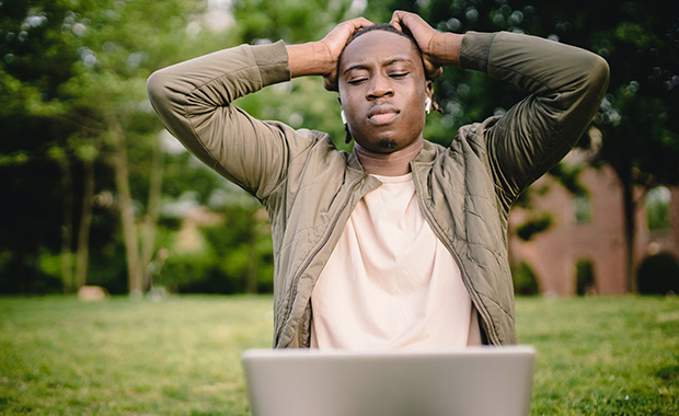 Man with laptop raising hands to head in frustration