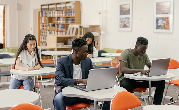 four students working at individual tables in library