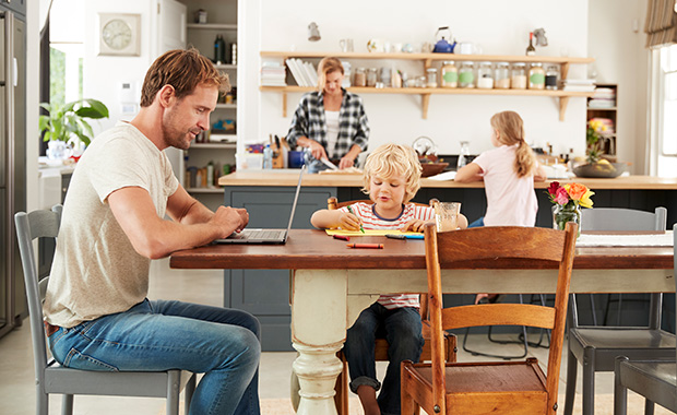 Family sits in kitchen with father working on laptop