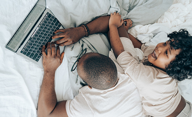 Father and child lying on bed looking at laptop