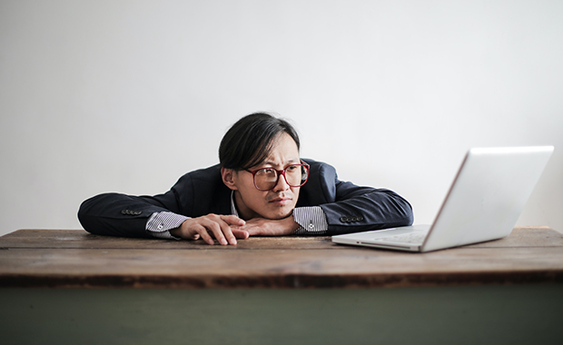 Man wearing glasses looks at computer in frustrated manner