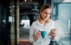 Businesswoman in office looking at smartphone during coffee break