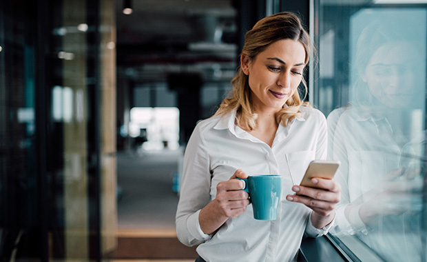 Businesswoman in office looking at smartphone during coffee break