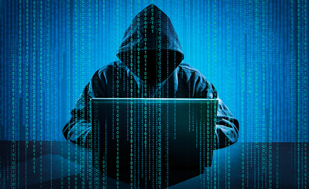 Hooded figure representing hacker types on laptop overlaid with binary code.