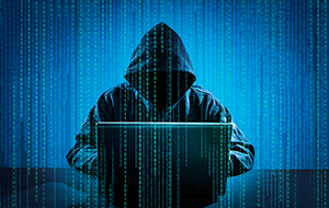 Hooded figure representing hacker types on laptop overlaid with binary code.