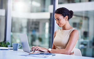 A woman sitting at her desk and smiling at her laptop.