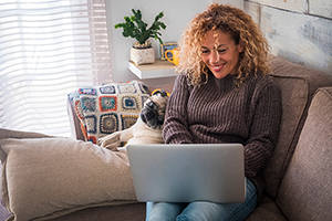 Woman and pug dog sit on couch looking at laptop