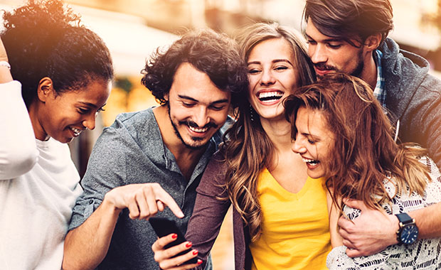 5 young people laughing while looking at a phone screen.