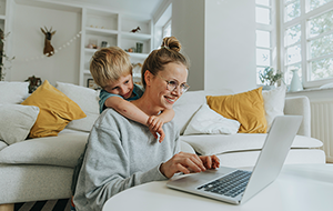 Woman works on laptop on coffee table with young boy looking over shoulder