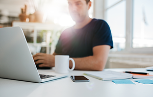 Blurred image of man at desk with laptop computer and smartphone