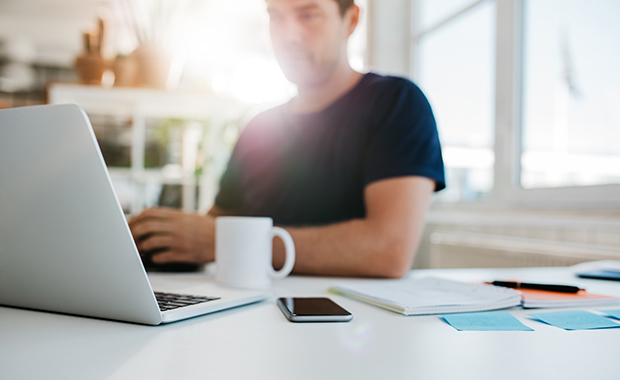 Blurred image of man at desk with laptop computer and smartphone