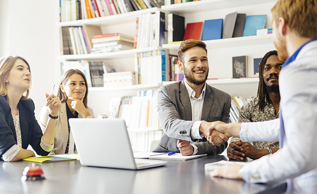 Group of young professionals welcomes new colleague with handshake