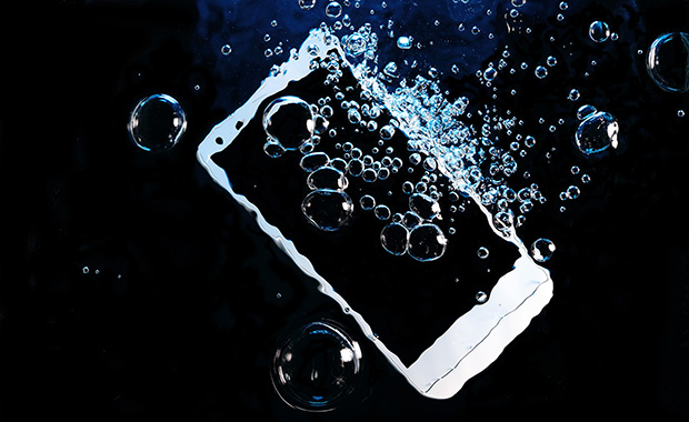 Smartphone submerged in dark water surrounded by air bubbles