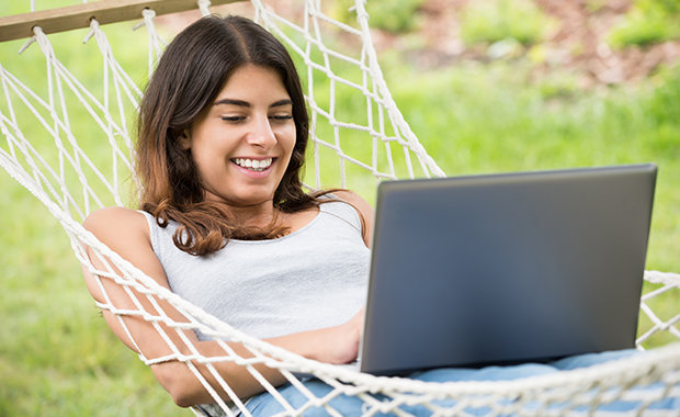 Smiling girl lies in hammock looking at laptop