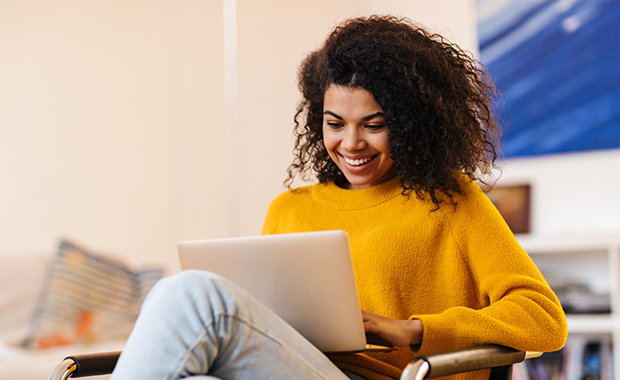 Smiling young Black woman sits looking at computer in lap