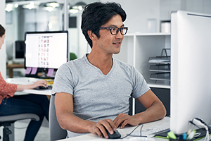 Smiling Asian man sitting in office looking at computer screen
