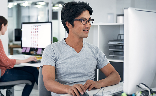 Smiling Asian man sitting in office looking at computer screen