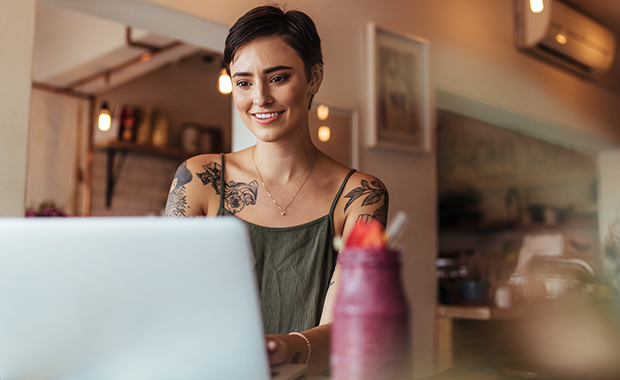 Smiling woman with tattoos looks at laptop in café